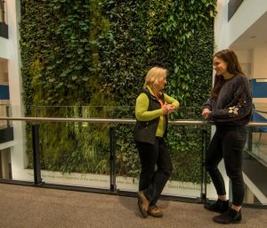 Two women chatting in front of a living wall 